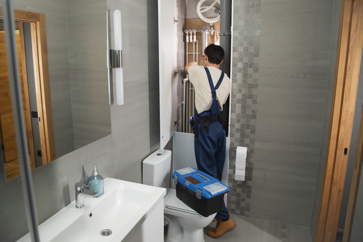 Plumber in overalls working on bathroom pipework with his toolbox